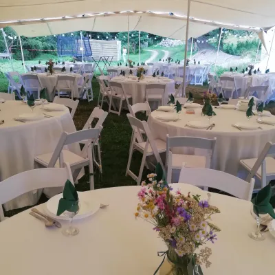 Nuntă în aer liber cu mobilier închiriat, mese rotunde și scaune albe Wimbledon, cu decor simplu cu flori de câmp
